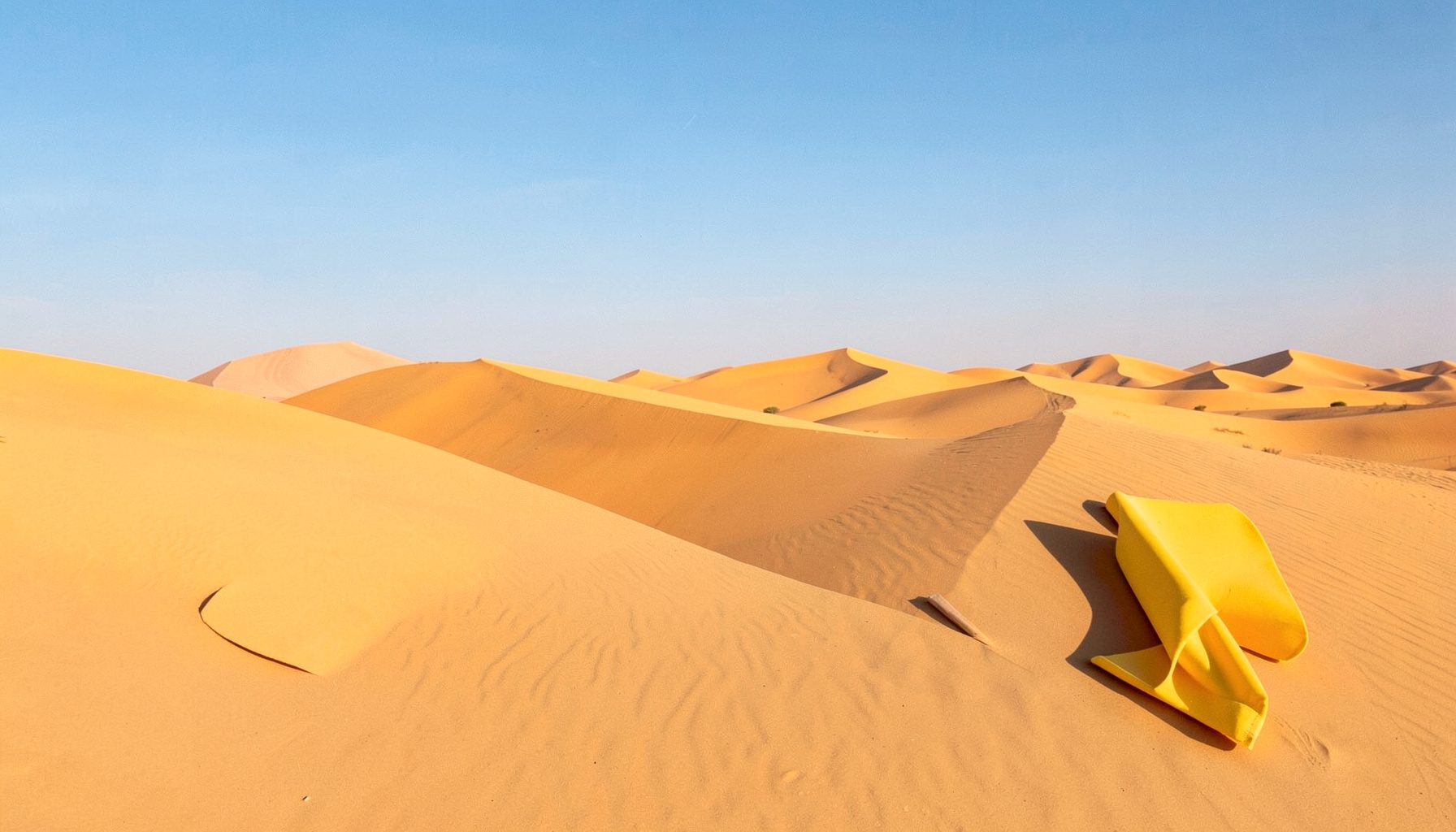 Wide landscape photograph of Rajasthan's golden desert dunes under a clear blue sky, with warm amber and sand tones dominating the scene